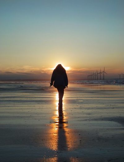 Silhouette woman on beach against sky during sunset