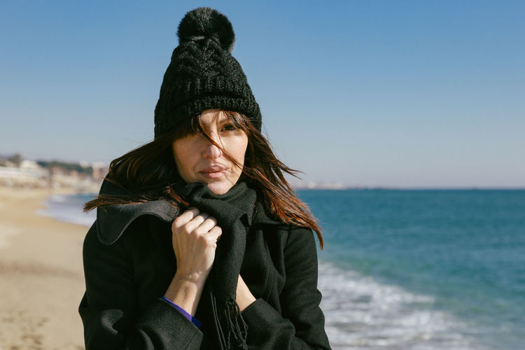 Portrait of beautiful woman with hat and coat on the beach on a sunny winter day