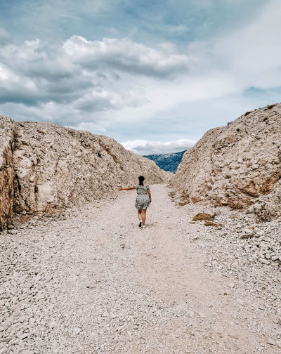 Rear view of young woman walking on gravel road in rocky canyon.