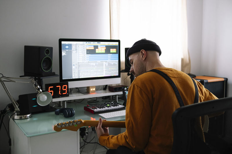 Freelancer with guitar sitting at table in home studio
