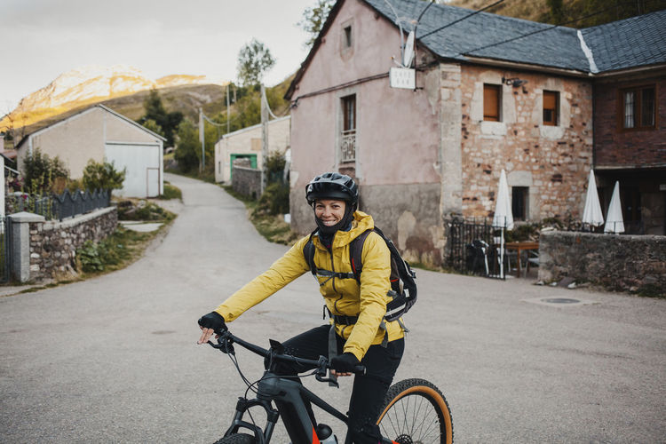 Mid adult woman in warm clothing riding mountain bike on road while traveling to somiedo natural park, spain