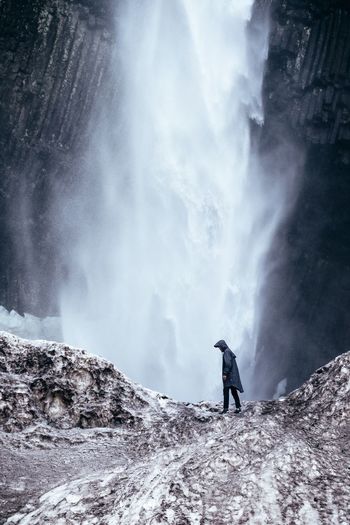 Man standing on rock by waterfall in forest