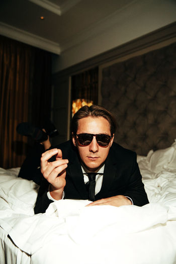 Young man wearing sunglasses while sitting on bed