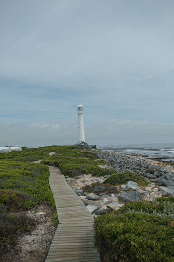 Footpath leading towards lighthouse by sea against sky