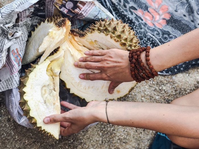 Cropped hands of woman holding durian at beach