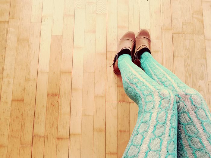 Low section of woman wearing turquoise stockings while sitting on hardwood floor