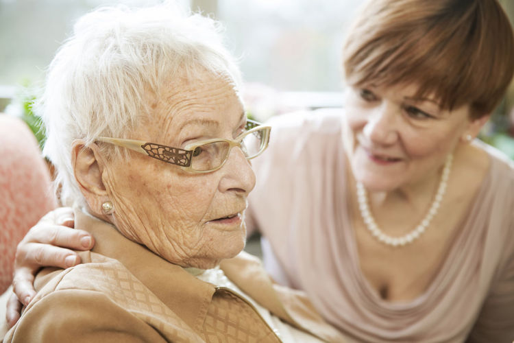 Portrait of senior woman with alzheimer's disease with her adult daughter watching in the background