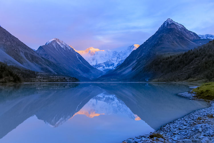 Snow-capped mountains and flowing lake in the evening at sunset