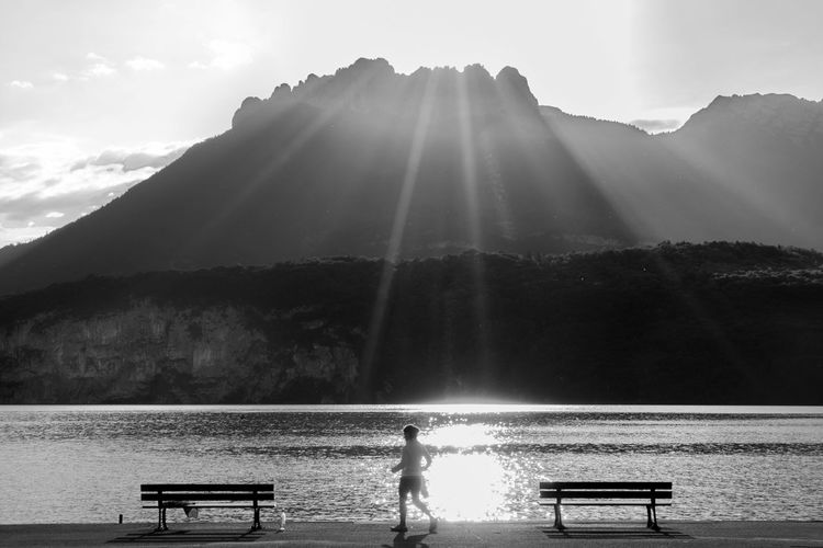 Woman walking on promenade by river against mountains during sunny day
