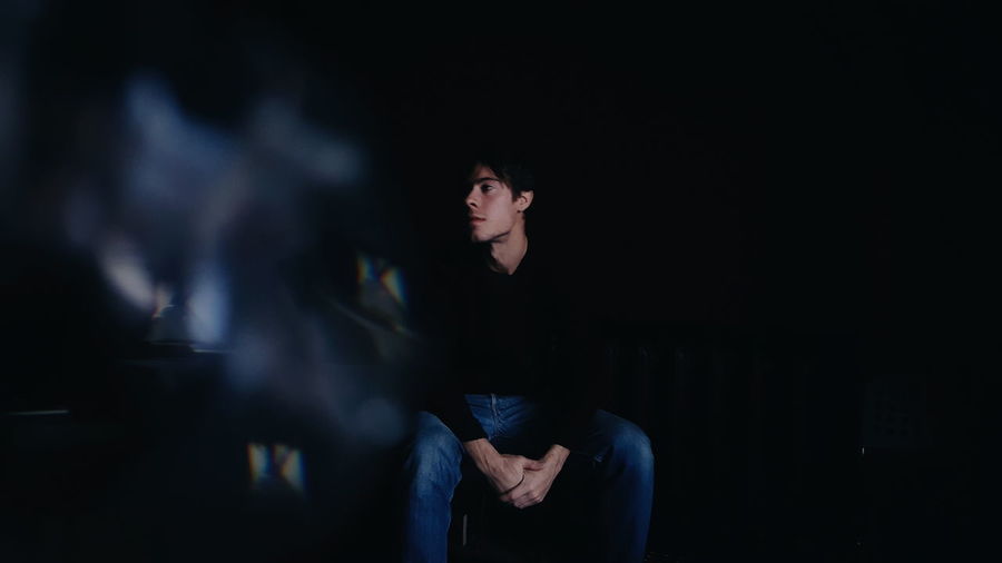 Thoughtful young man looking away while sitting on chair in darkroom