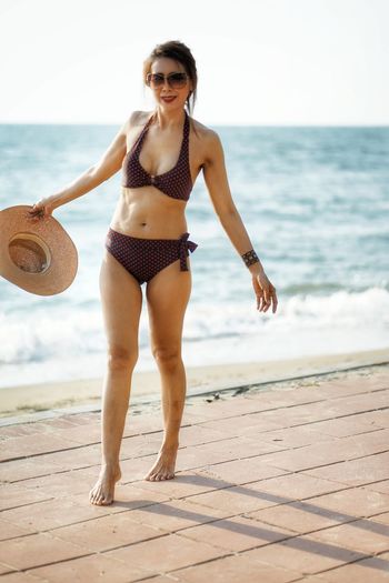 Portrait of sensuous woman in bikini wearing sunglasses while standing at beach