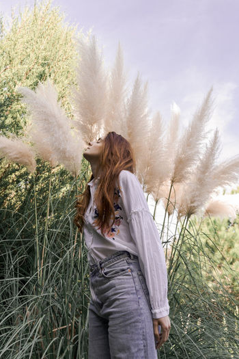Young redhead woman standing by pampas grass in garden