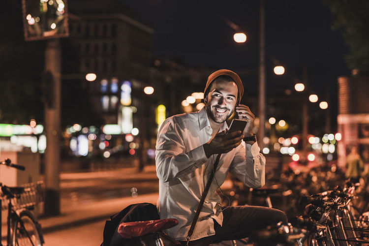 Young man in the city with eardphones and cell phone at night