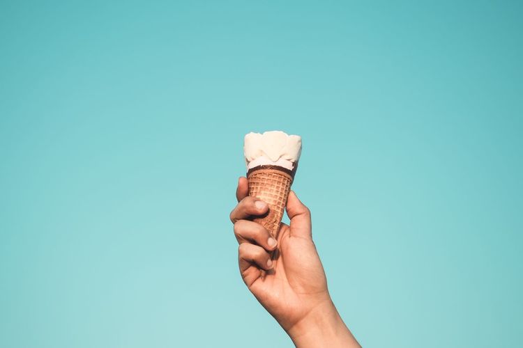 Human hand holding ice cream against blue background