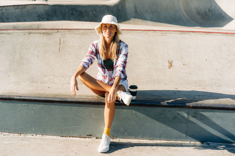 Stylish woman in a panama hat sits in a skatepark on a summer day.