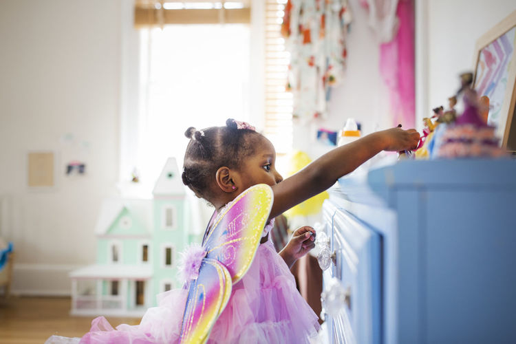 Side view of girl dressed in fairy costume playing with toys at home