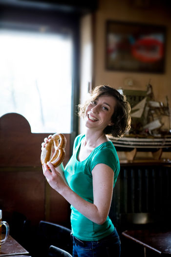 Portrait of smiling mid adult woman holding pretzel at home