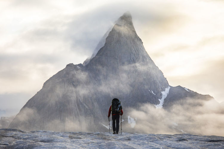 Rear view of backpacker approaching dramatic mountain.