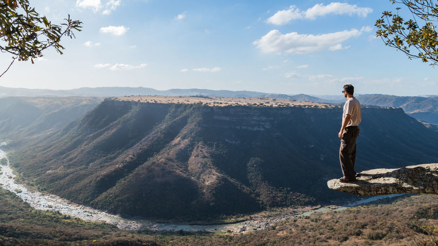 Man standing on cliff by mountains against sky at oribi gorge