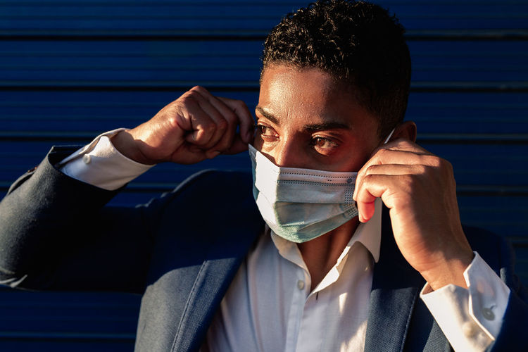 Young african american male in formal outfit putting on medical mask for coronavirus prevention