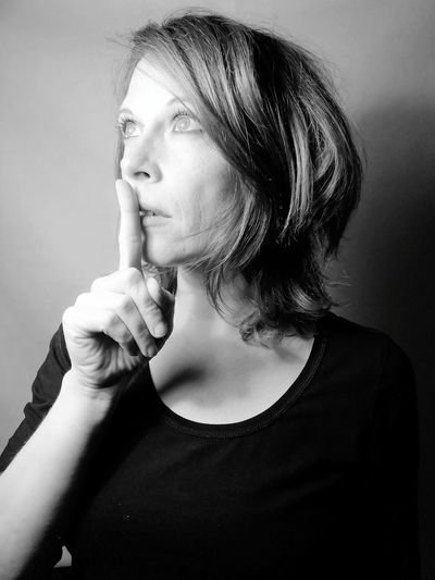 Woman with finger on lips standing against wall