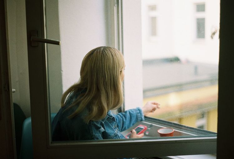 Close-up of girl using mobile phone in window