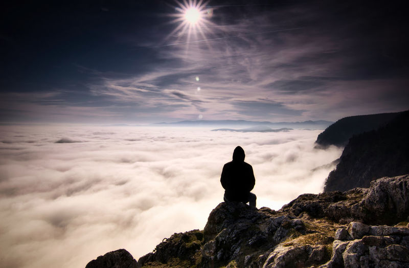 Rear view of silhouette man sitting on mountain against sky