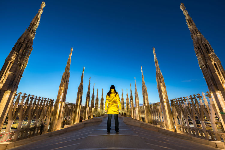 Rear view of woman standing on historic bridge against clear blue sky at dusk