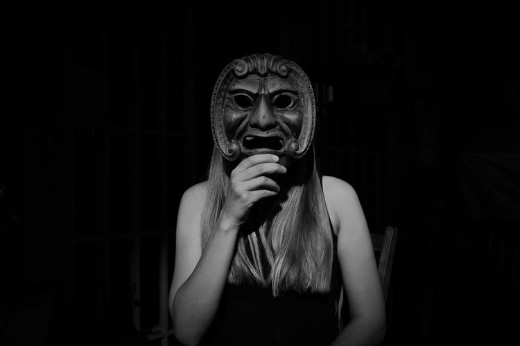 Woman covering face with mask against black background