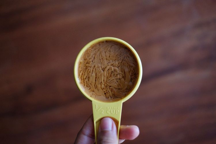 Person holding peanut butter in measuring cup