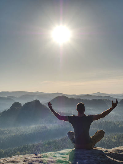 Rear view of man with arms outstretched in yoga pose on mountain against sky