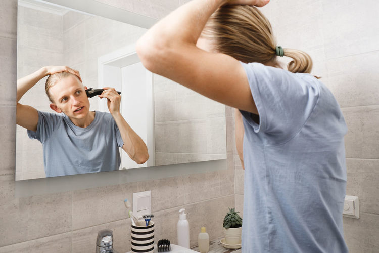 Personal hygiene, caucasian man cutting his own hair in the bathroom with wireless electric shaver