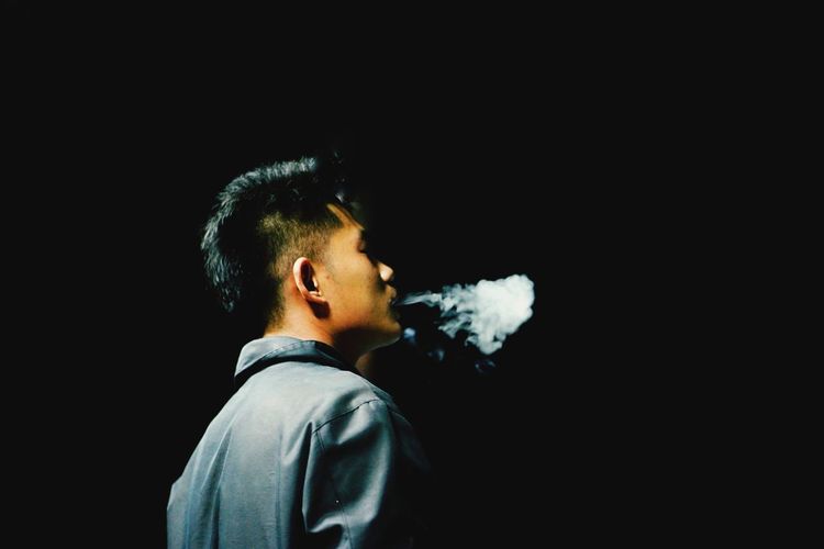 Side view of man smoking against black background