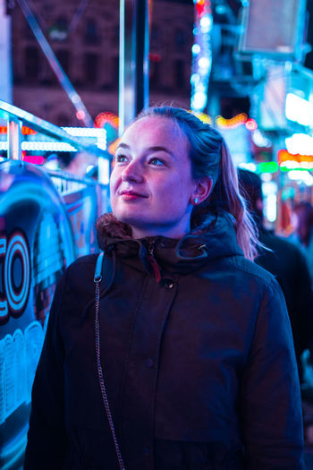 Close-up of young woman standing against illuminated amusement ride at night