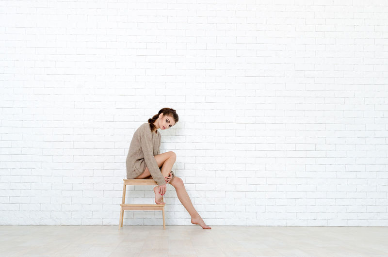 Portrait of woman sitting against white wall