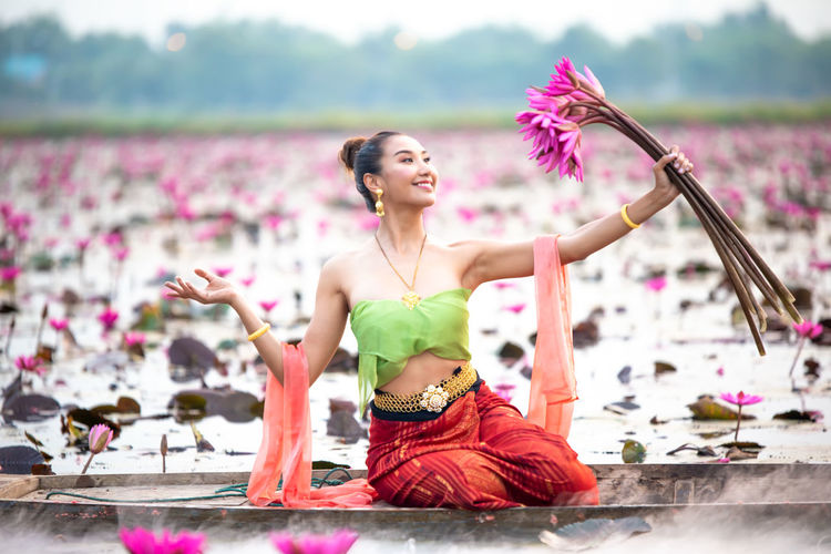 Smiling young woman holding water lilies in boat on lake