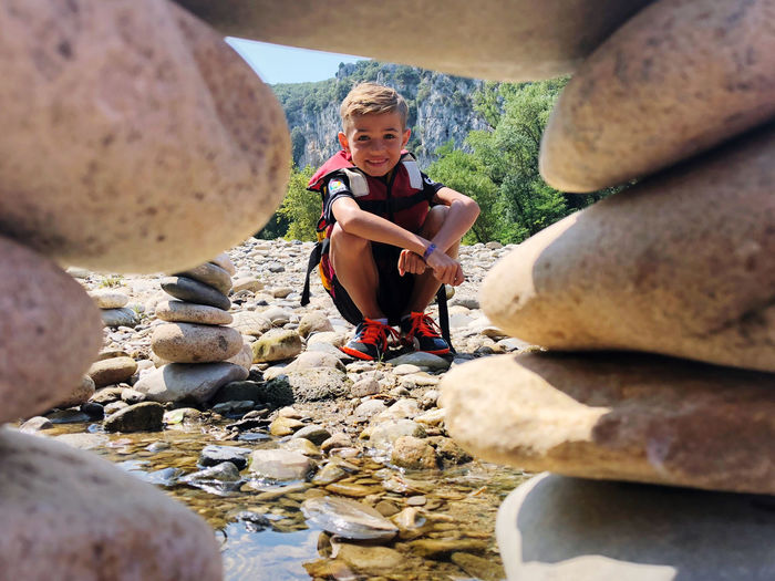 Portrait of cute boy crouching on land seen through rocks