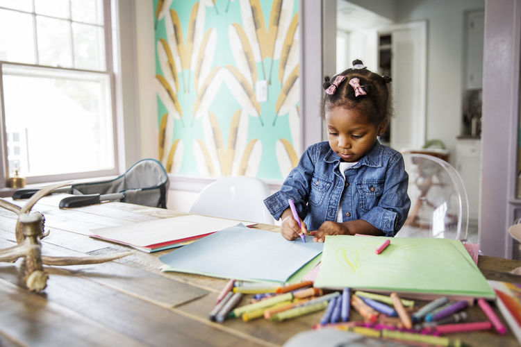 Cute girl coloring with crayon in book on table at home