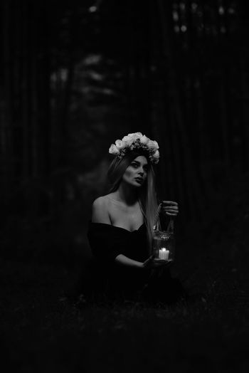 Young woman holding candle in jar standing at forest