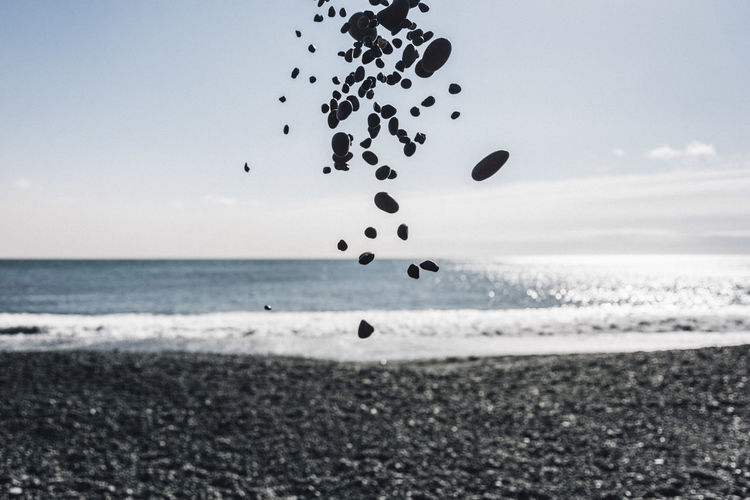 Stones in mid-air at beach against sky