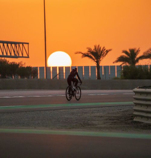 A female cyclist in training session and a beautiful sunset in the background. 