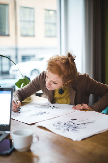 Confident female illustrator drawing on paper at table in office