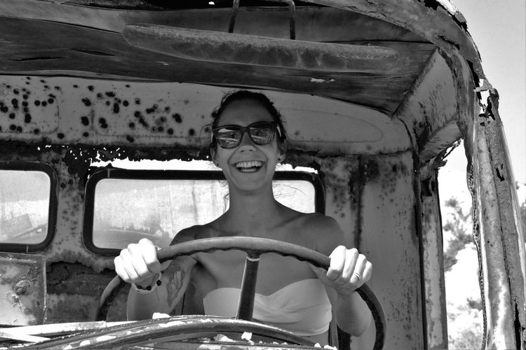 Portrait of happy woman sitting in old abandoned car