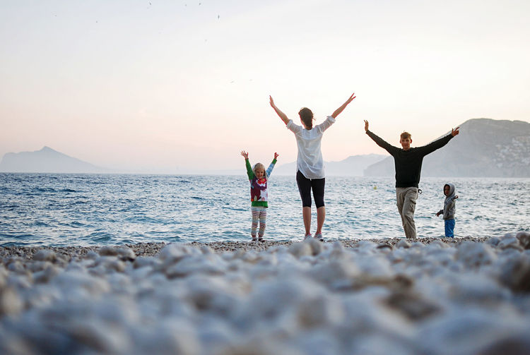 Rear view of family with two kids with arms outstretched standing at beach