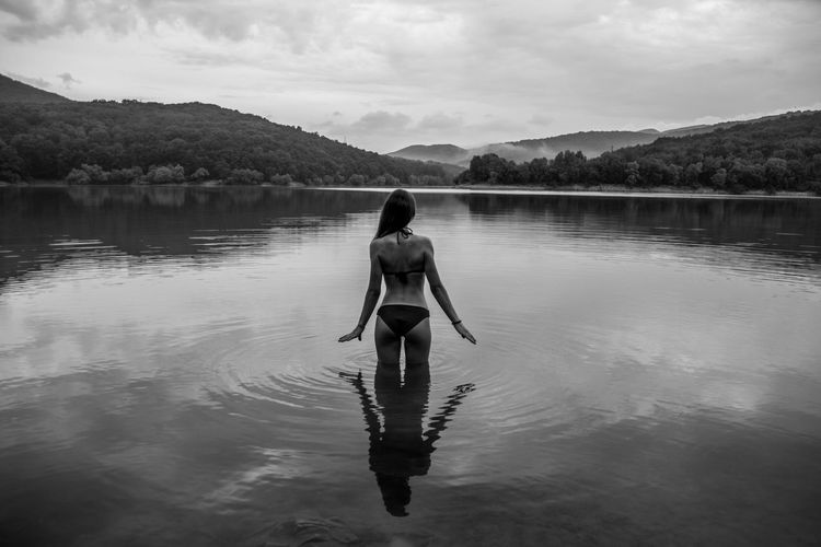 Rear view of woman standing in lake against sky
