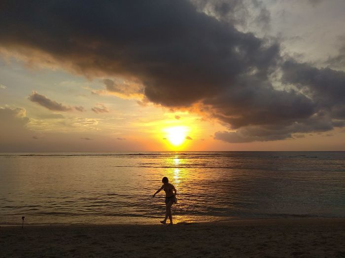 Silhouette person on beach against sky during sunset