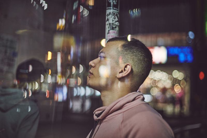 Portrait of young man looking at illuminated city at night with lots of reflections and bokeh