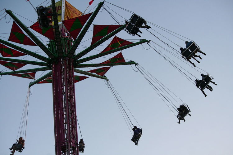 Low angle view of people on chain swing ride against clear sky
