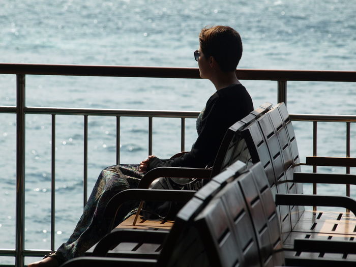 Side view of woman sitting on bench by sea