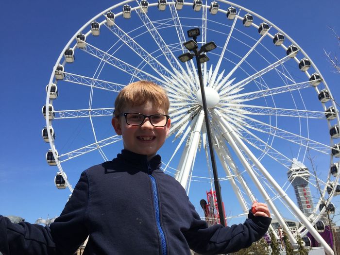 Low angle portrait of smiling boy standing against ferris wheel